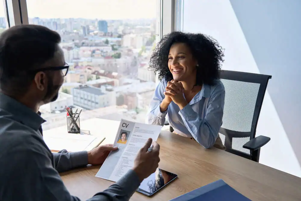 A professional job interview at a high-end Ocala hotel featuring a smiling female candidate with curly hair and a male recruiter holding a CV in a modern office with a city view for Engagement Survey ROI.