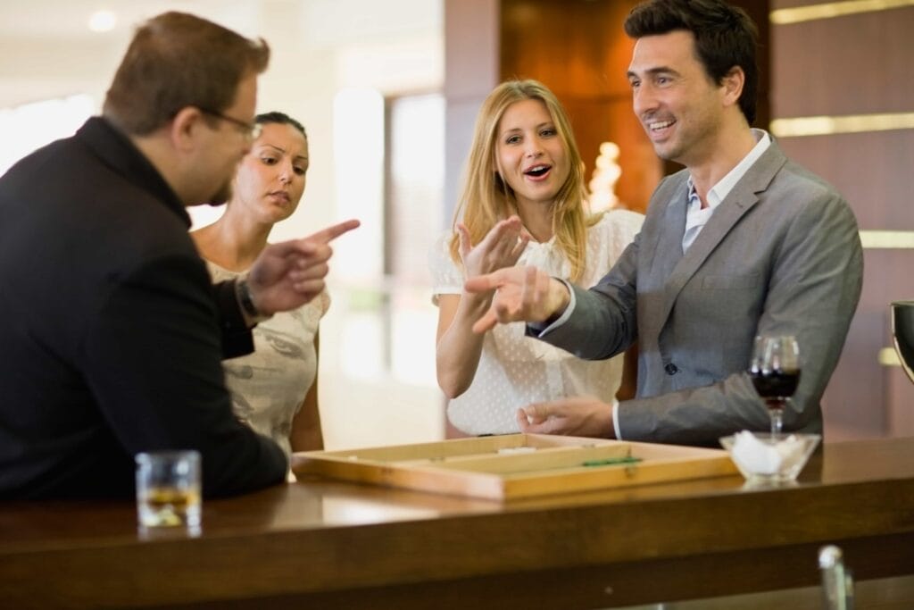 Friends laughing and playing a competitive game of backgammon at an upscale hotel bar with craft drinks in Los Angeles, California.