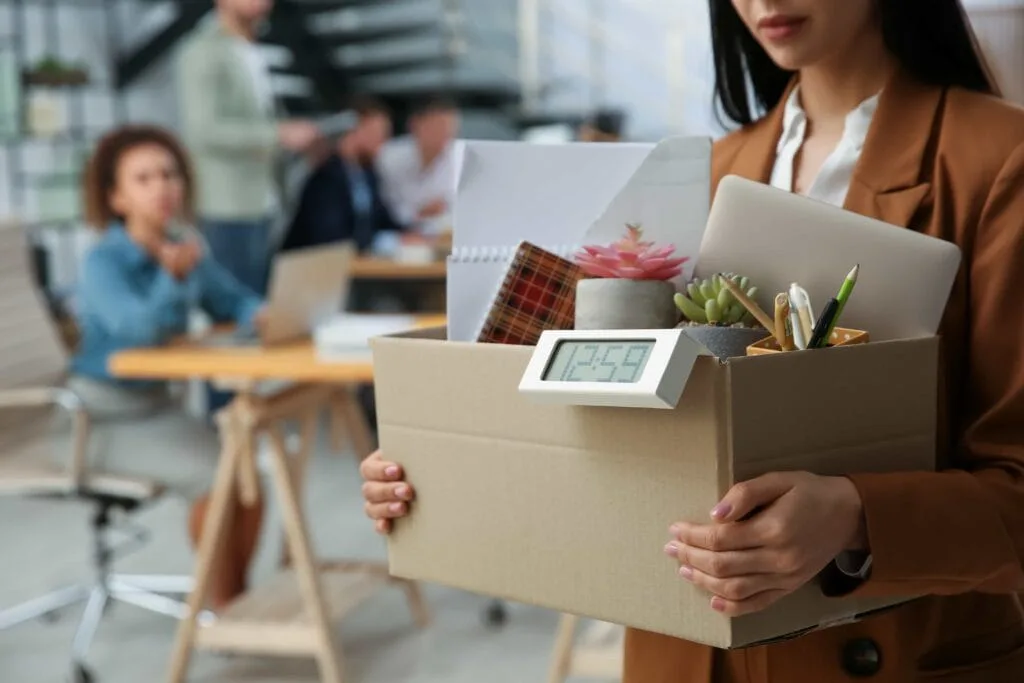 A professional woman carrying a cardboard box filled with office supplies, representing employee turnover and career transition services in Central Florida.