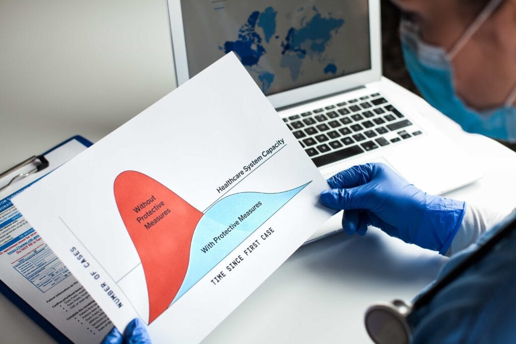 A medical professional in blue gloves holding a chart comparing virus spread with and without protective measures to manage healthcare system capacity in Central Florida.
