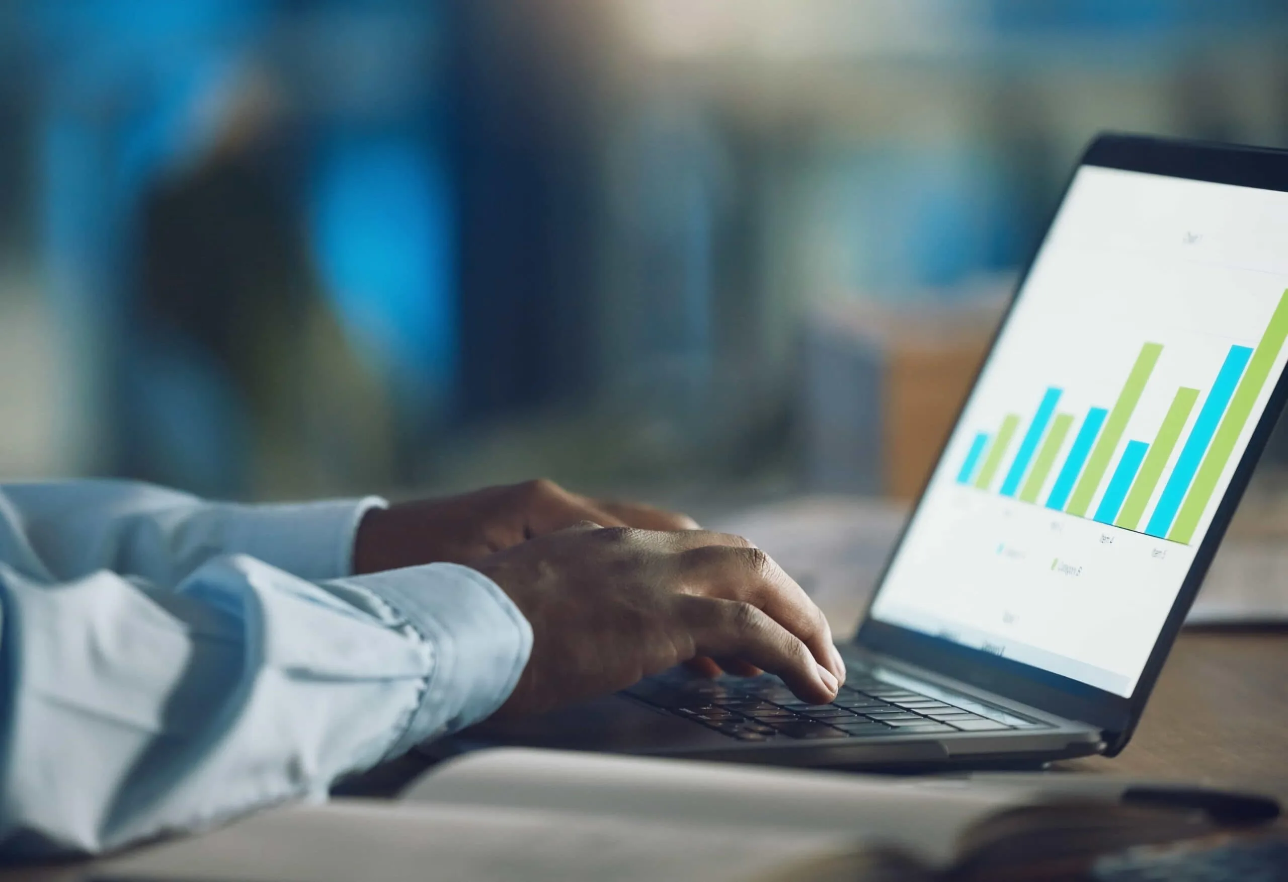 A close-up shot of an analyst's hands typing on a laptop keyboard while reviewing financial growth bar charts during a business enterprise employee analytics analytics consulting session in New York, NY.