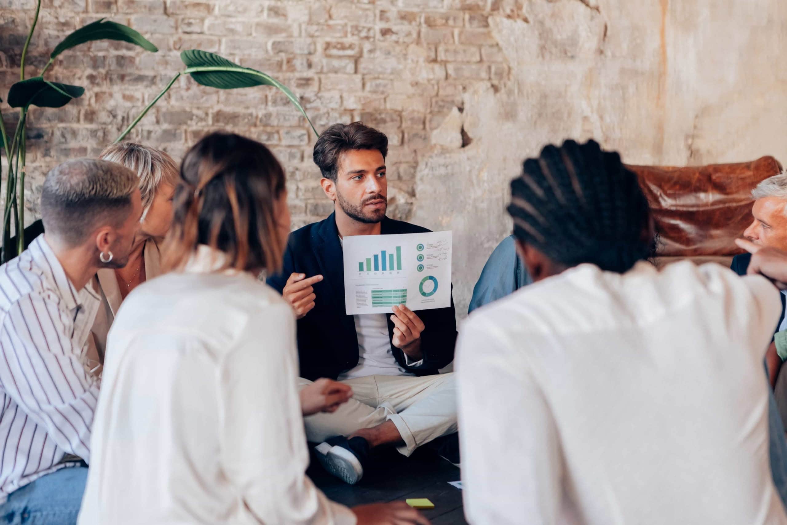 A business consultant holding up a printed report with employee survey data charts and graphs during a strategic team meeting with colleagues in a modern, urban office setting in Denver, Colorado.