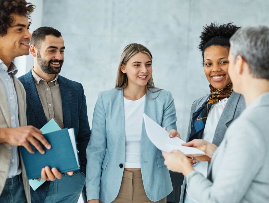 A diverse team of young business professionals in a modern office, reviewing documents and discussing Culture Amp survey questions in Boston, MA.