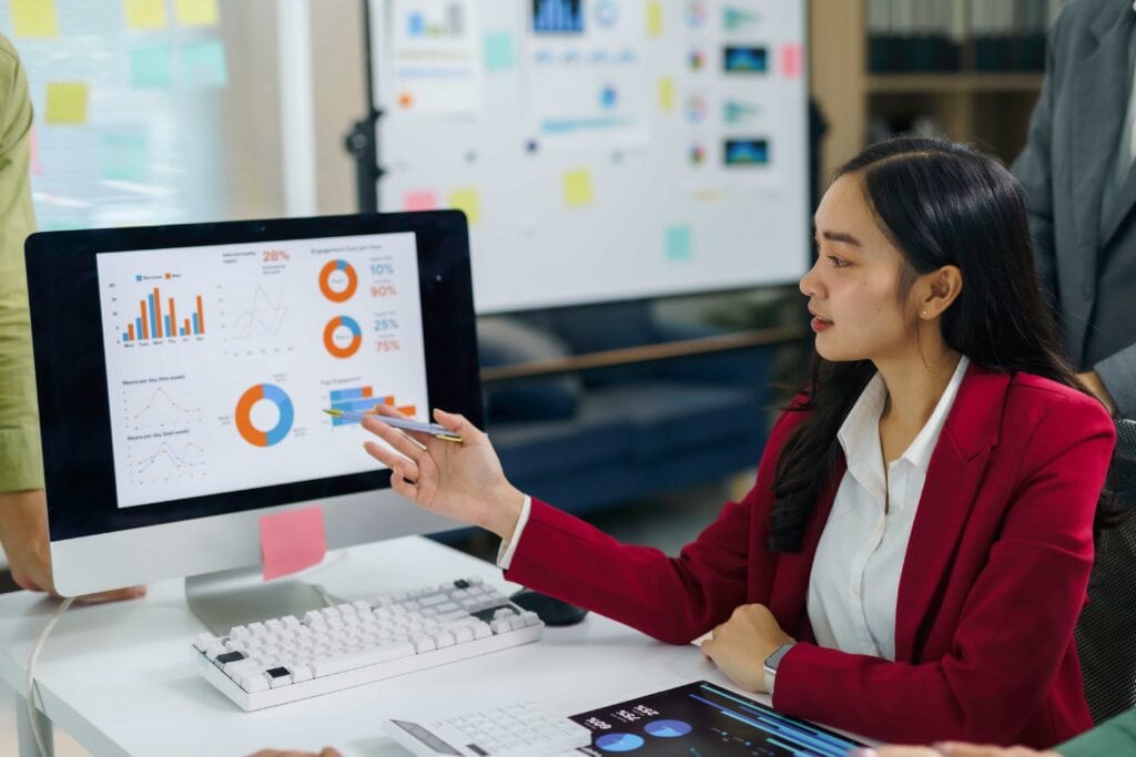 A businesswoman in a red blazer presenting Culture Amp survey data analysis on a computer screen to her team in San Francisco, CA.