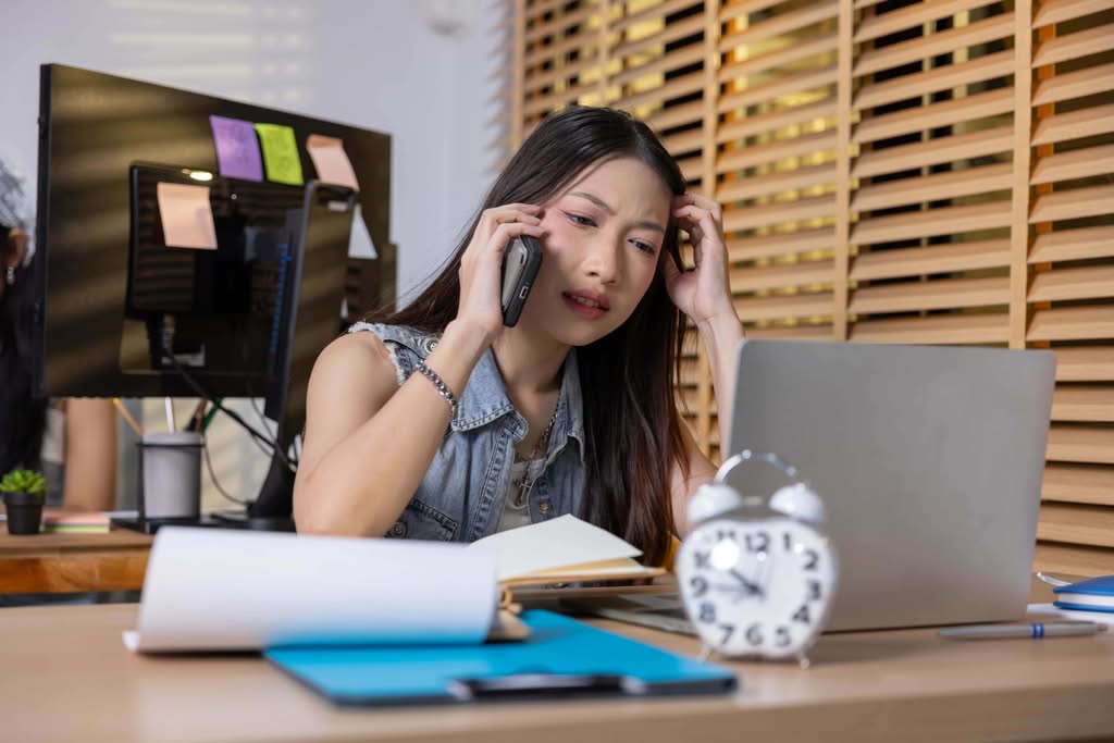 A stressed young woman talking on her phone at a front desk, representing hospitality burnout management challenges in Las Vegas, NV.