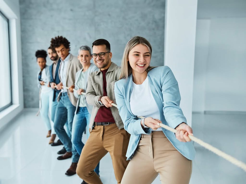A diverse group of young corporate professionals smiling and frontline staff retention laughing while participating in a collaborative tug-of-war exercise during a workplace alignment workshop in Denver, CO.