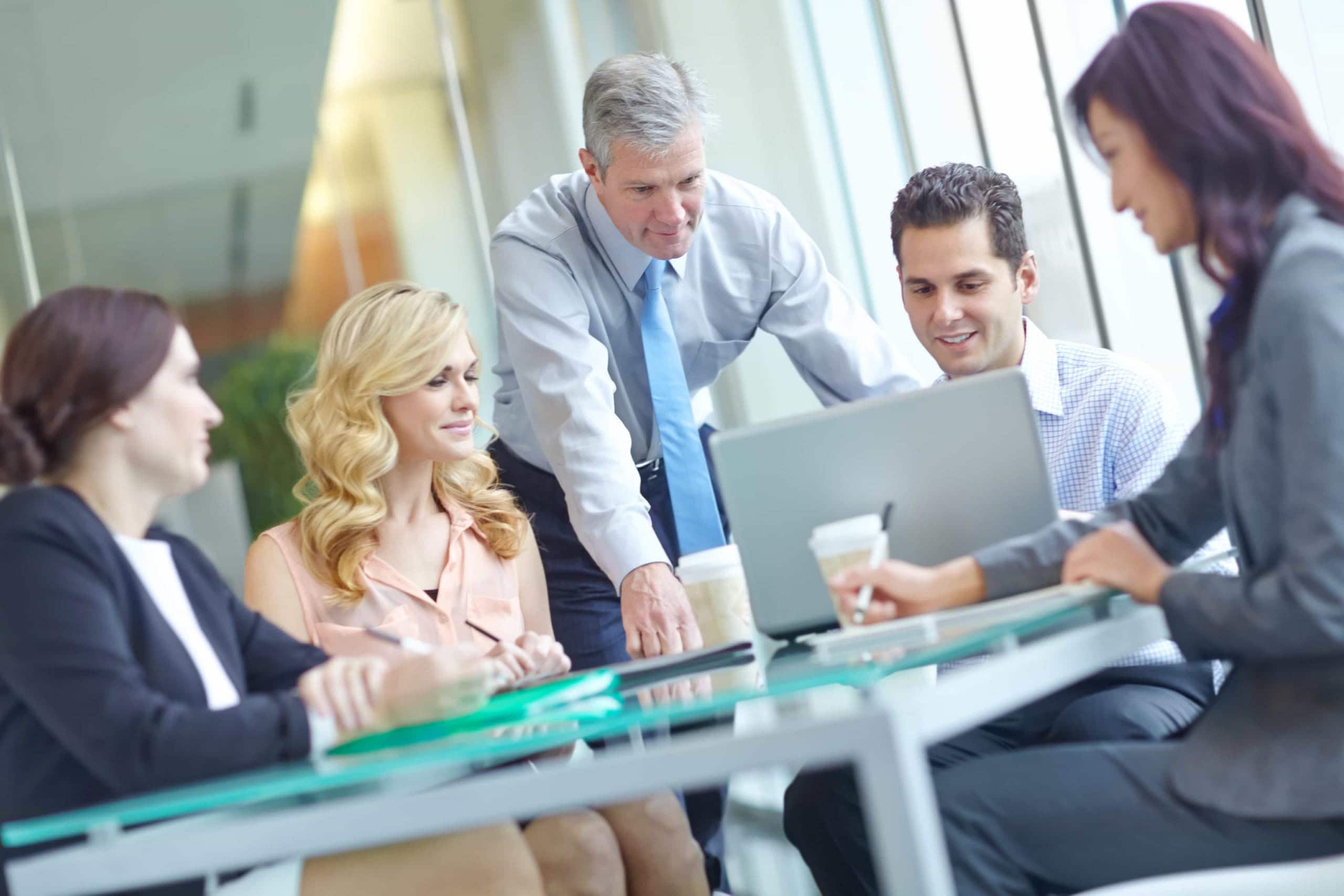 A diverse corporate business team collaborates around a modern glass table with a laptop during a strategic South Florida HR Consulting session in Miami, FL.